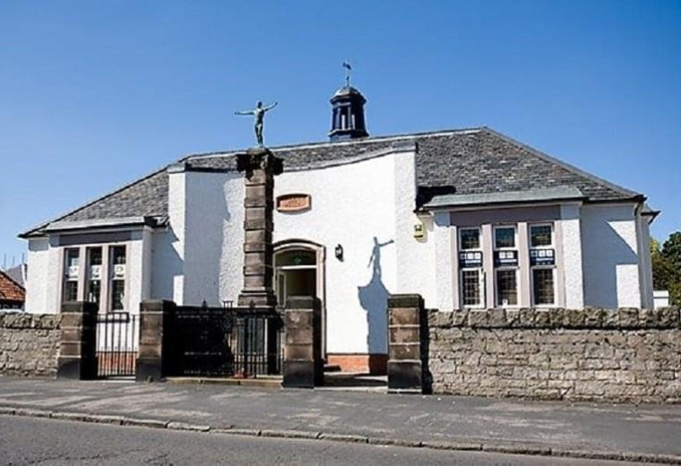 Exterior view of Cockburn Halls, George Street, Ormiston, East Lothian, Scotland featuring a statue and stone wall.