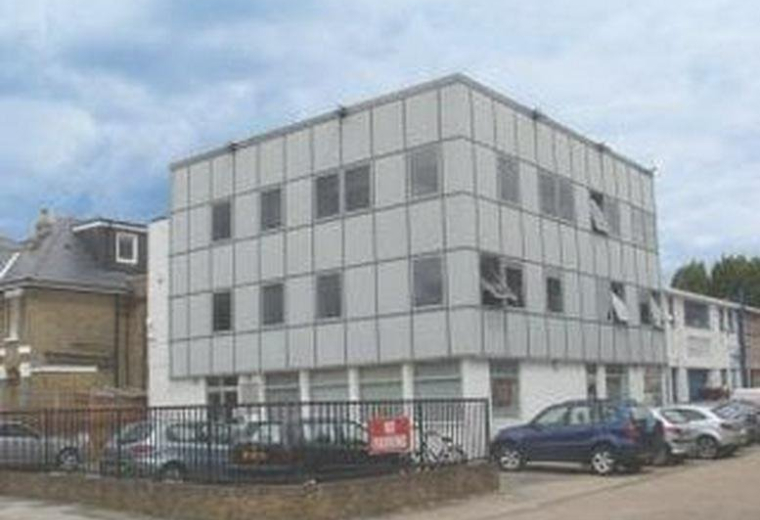 Exterior view of the grey paneled facade of Epic House with parked cars in front.