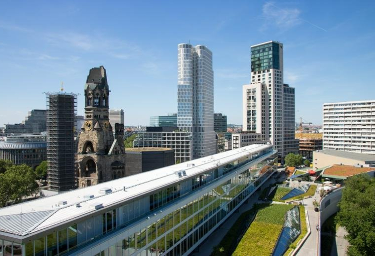 Exterior view of the Kurfürstendamm 11 building featuring the Kaiser Wilhelm Memorial Church and modern skyscrapers.