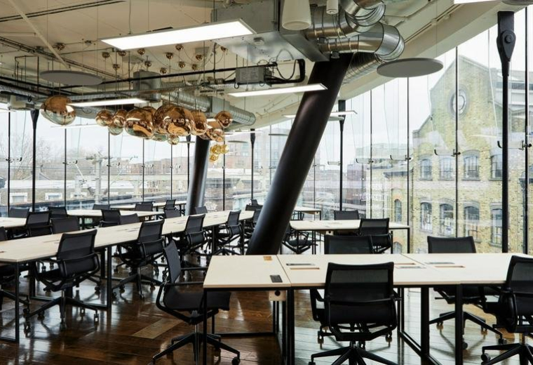 Spacious open-plan workspace with multiple desks, floor-to-ceiling windows and city views.