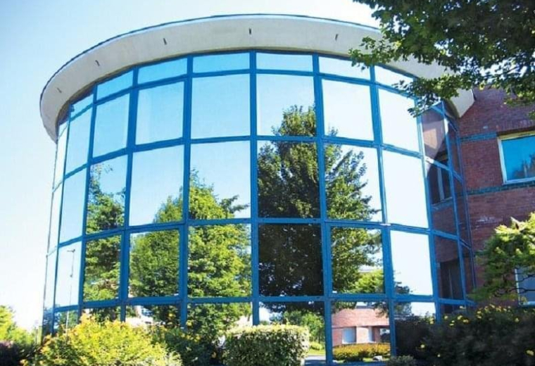 Curved glass exterior of Villeneuve d'Ascq, 1-3 Allée Lavoisier reflecting trees and blue sky.