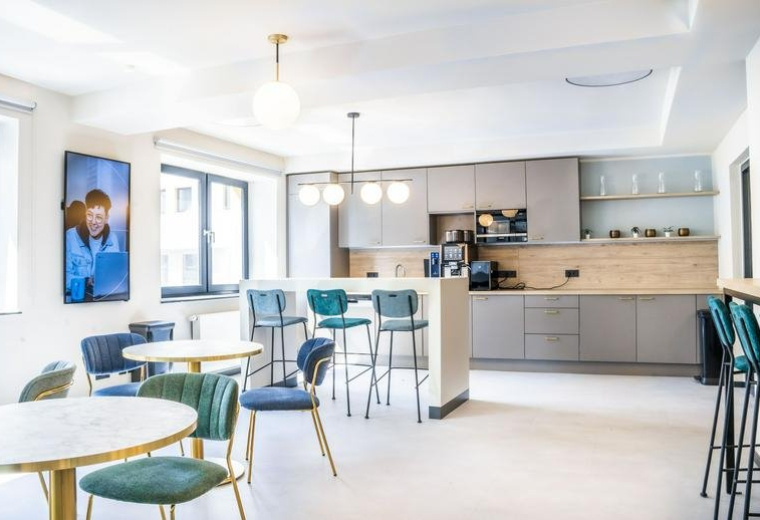 Modern communal kitchen and cafe area with teal chairs and light wood accents.