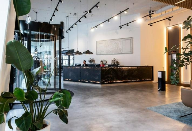 Spacious reception area at Prins Alexanderplein 8 featuring a dark textured desk, high ceilings, and indoor plants.