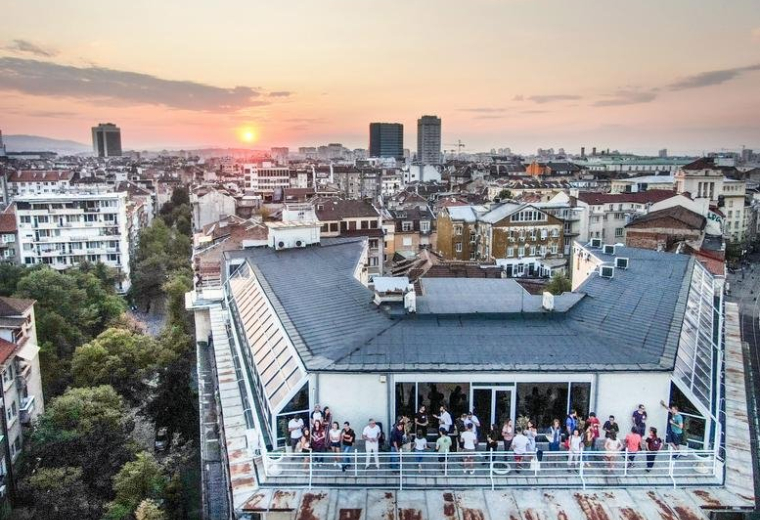 Rooftop view of the Sofia Center building at sunset with a terrace full of people.