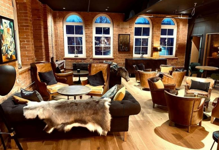 Spacious communal lounge at The Tannery featuring leather armchairs, arched windows, and a faux fur throw.