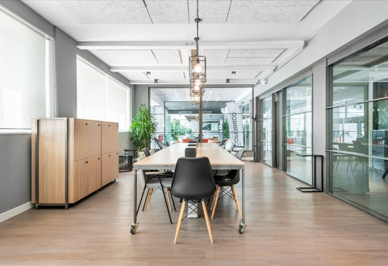 Open-plan office area at Viale Monza, 259/265 with a long wooden desk and glass-partitioned meeting rooms.