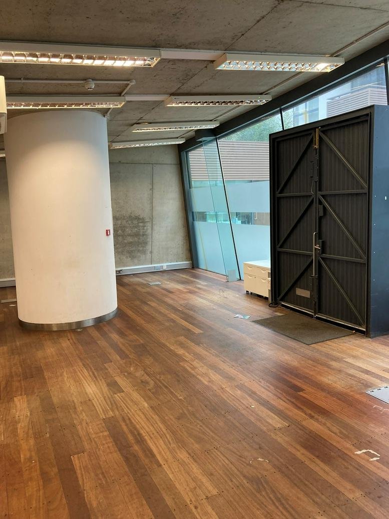Spacious empty office with large black industrial doors, hardwood flooring, and glass partition walls.