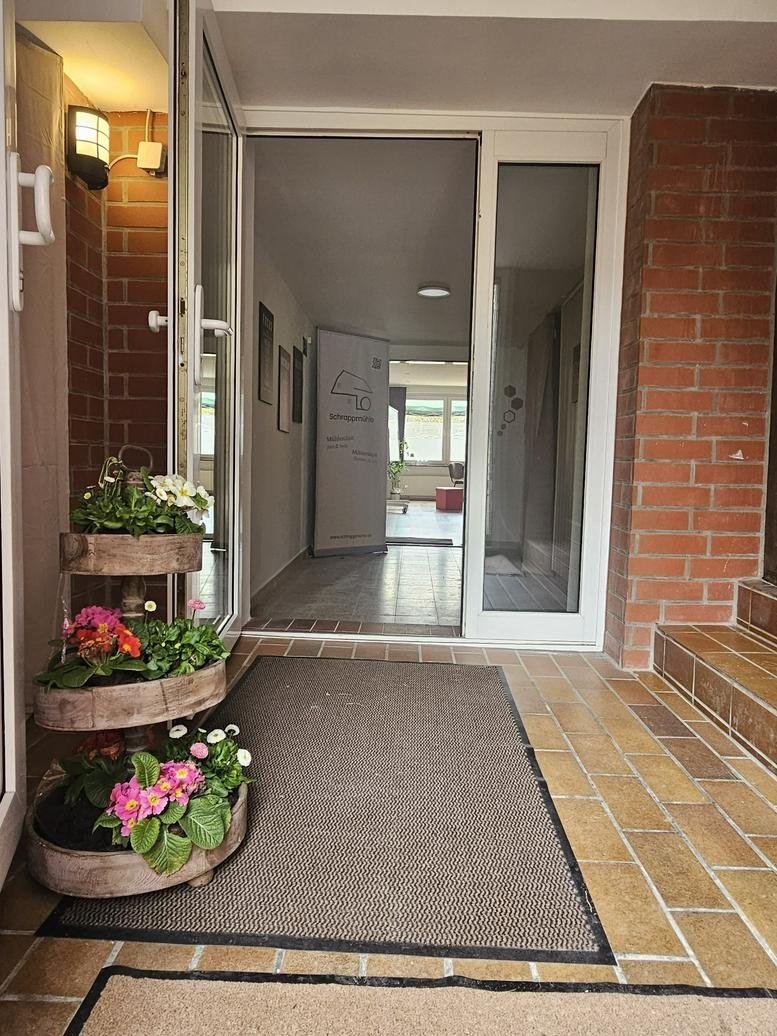 Building entrance of 1, Schrappmühle with tiered flower planters and a welcoming mat.