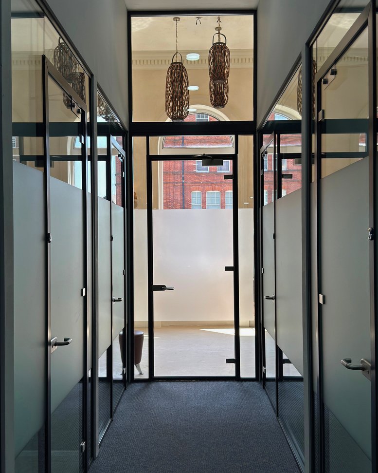Bright hallway at 106, Finchley Road with glass-walled suites and decorative hanging lamps.