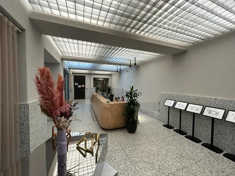 Spacious modern lobby at 117, Chausseestraße featuring a curved wooden reception desk and a grid-patterned light ceiling.