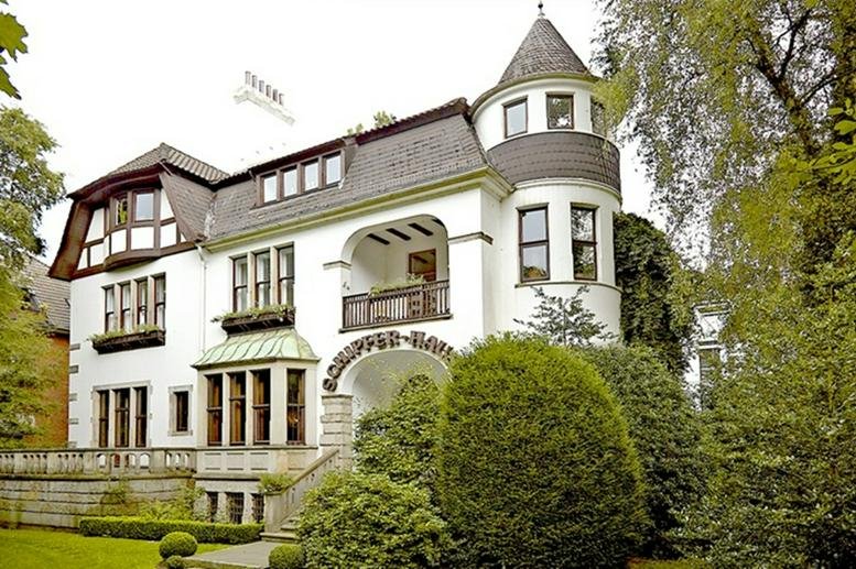 Exterior view of the historic white villa at 117, Parkallee, featuring a turret and lush gardens.