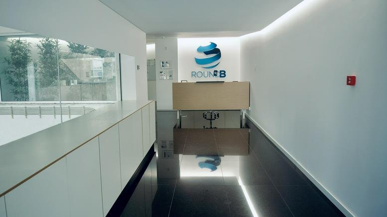 Sleek modern reception area at 11B, Rua Amílcar Cabral, with a wood-fronted desk and logo wall.