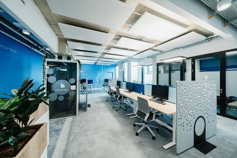 Spacious open-plan workspace at 12, Koppstraße with modern desks, acoustic ceiling panels, and blue accent walls.