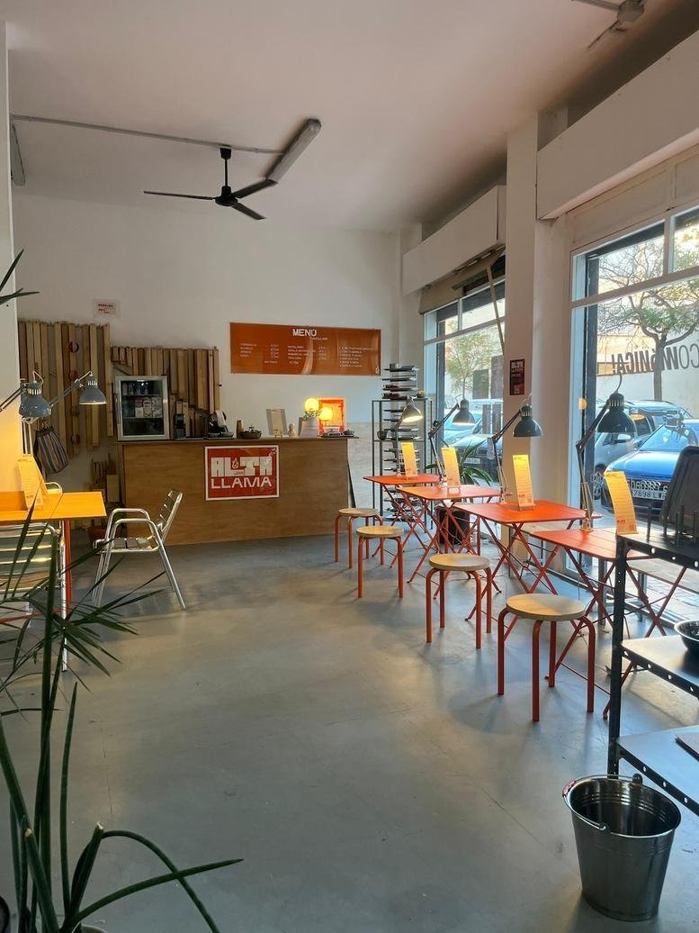 Bright open-plan coworking space with orange cafe tables, wooden stools, and a reception desk.