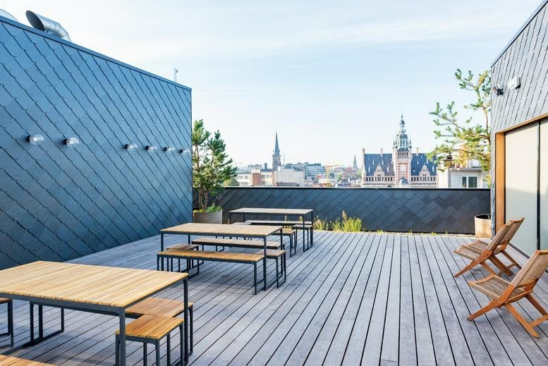 Spacious rooftop terrace with wooden tables, benches, and views of the city skyline.