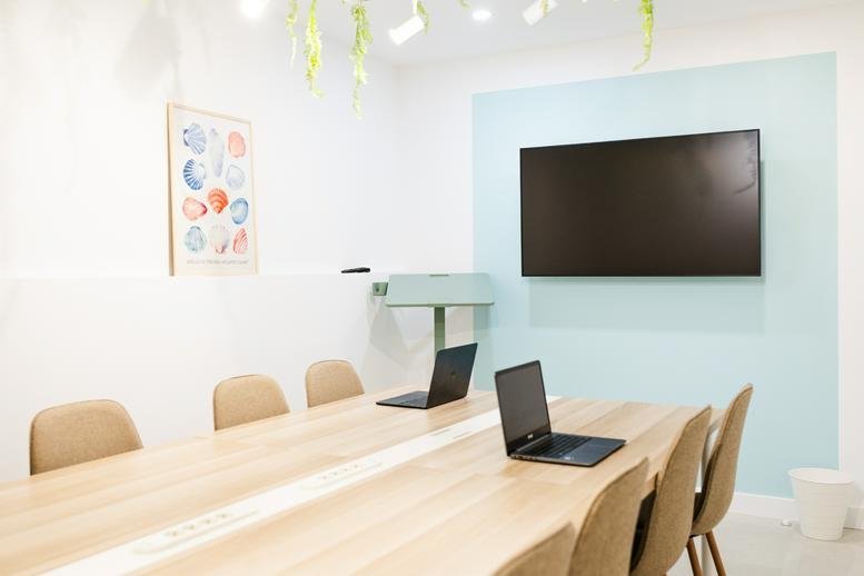 Bright conference room with a large screen, light wood table, and ergonomic chairs.