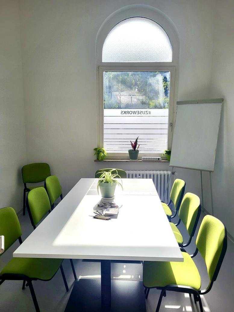 Bright, modern meeting room with a large white table, green chairs, and an arched window at 15, Bahnhofstraße.