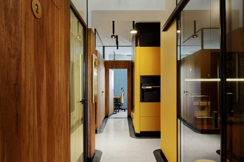 Hallway at 152 Puławska with warm wood paneling, glass partitions, and vibrant yellow cabinetry.