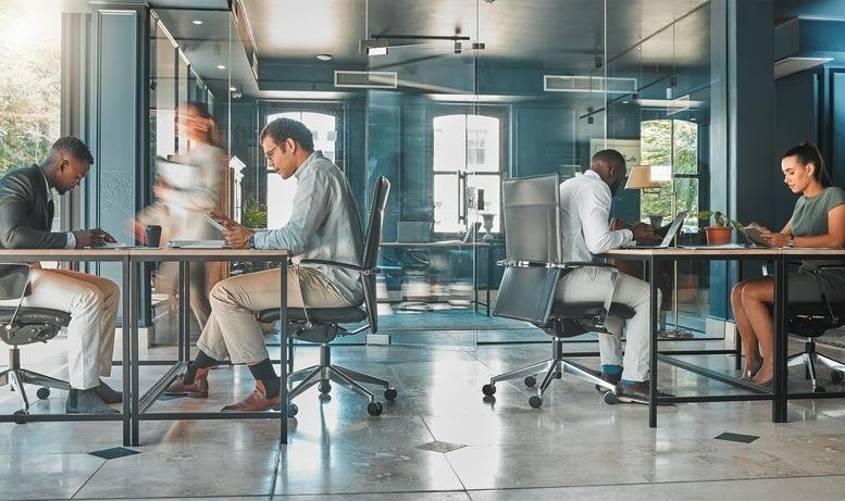 Spacious industrial-style open-plan office at 16, Denman Street with employees working at large communal desks.