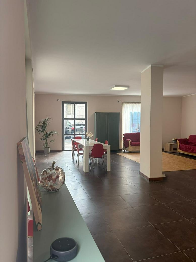 Spacious communal dining area at 16, Via Giuditta Pasta, featuring a white table, red chairs, and a decorative apple.