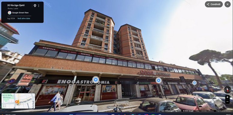 Street-level view of the brick mixed-use building at 16, Via Ugo Ojetti with retail shops and residential balconies.