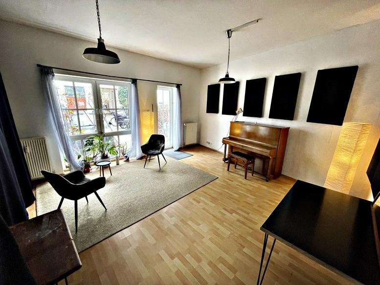 Bright multi-purpose room featuring soundproofing panels, a piano, and lounge seating.