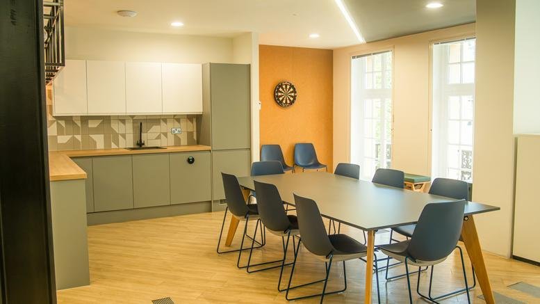 Spacious communal kitchen and dining area at 180, Great Portland Street with a feature dartboard and green cabinetry.