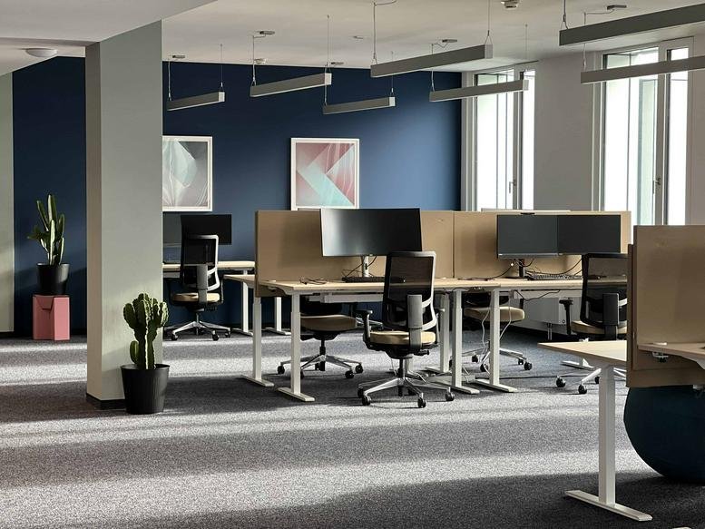 Spacious open-plan workspace at 18a, Zeppelinstraße with modern desks, ergonomic chairs, and blue feature walls.