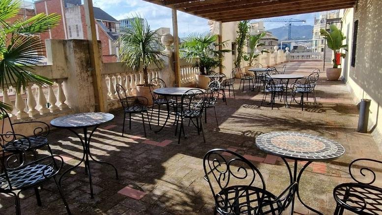 Spacious rooftop terrace at 190, Carrer de Pau Claris with bistro tables and potted palm trees.