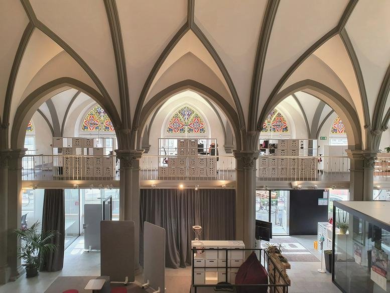 Bright, open-plan workspace at 1B, Brückengasse featuring dramatic Gothic arches and mezzanine levels.