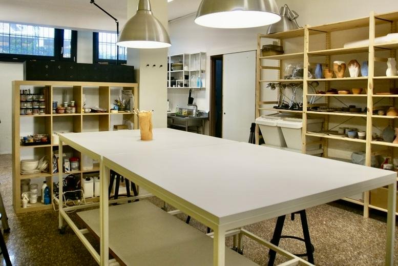 Spacious studio at 2, Via Giuseppe Biancardi with a large white central work table and wooden shelving.