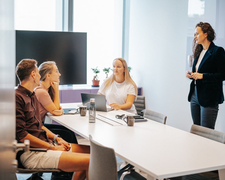 Professional team meeting in a bright conference room with a large wall monitor.