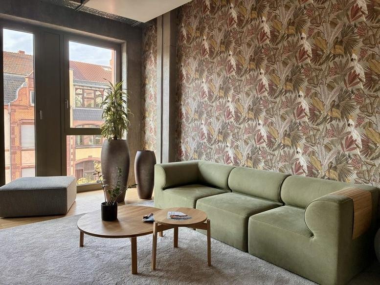 Bright breakout area at 23, Rintheimer Straße,Gebäude A, with a green sofa, patterned wallpaper, and potted plants.