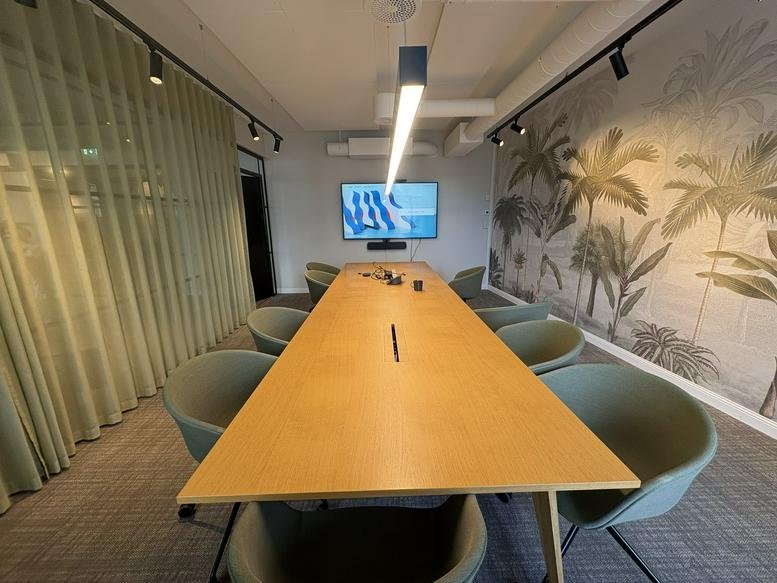 Spacious meeting room at 24, Hegdehaugsveien, featuring a long light wood table and tropical palm leaf mural.