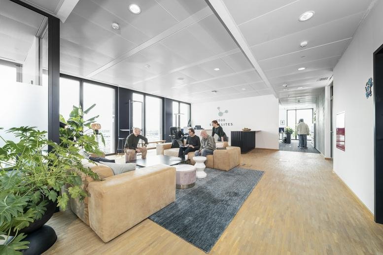 Spacious breakout lounge with tan sofas, indoor plants, and a blue patterned rug.