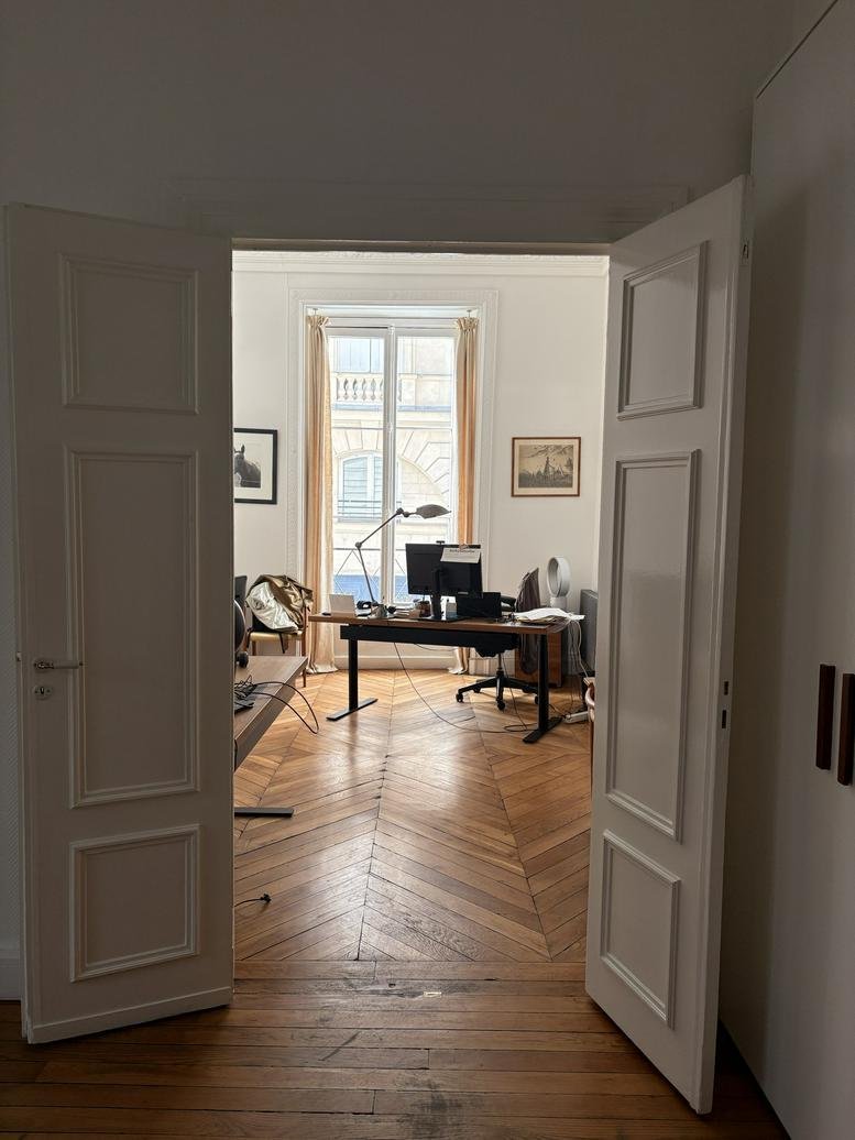 Entryway view of an office at 26, Rue de Richelieu, featuring chevron wood floors and tall windows.