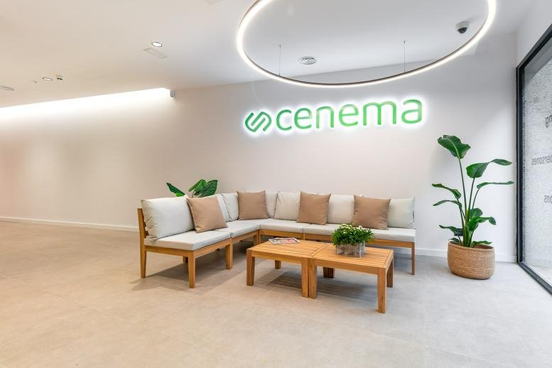Reception area at 261, Carrer de Sardenya with a wooden L-shaped sofa, green plants, and branded signage.