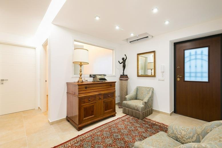 Spacious reception area at 28, Via Pietro Ferrigni featuring a wooden dresser and patterned rug.