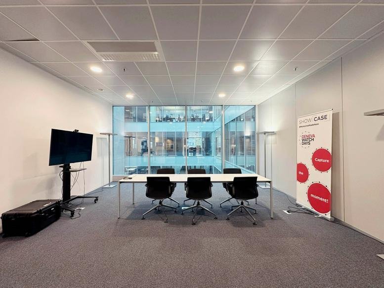 Meeting room at 3, Chemin du Pré-Fleuri with a white conference table, black chairs, and a large display screen.