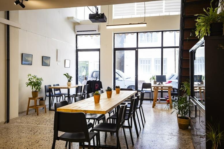 Spacious communal coworking area with long wooden tables, plants, and natural light at 30, Σμύρνης.