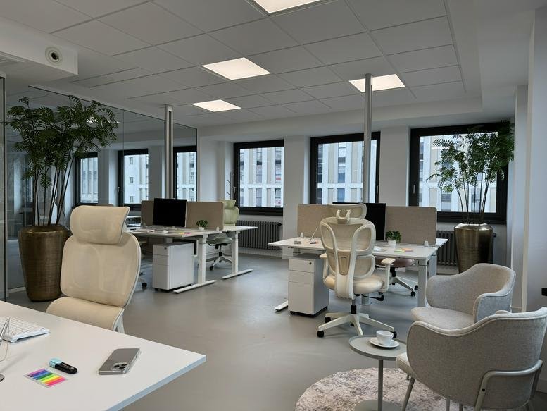 Spacious open-plan office with white height-adjustable desks and ergonomic seating.