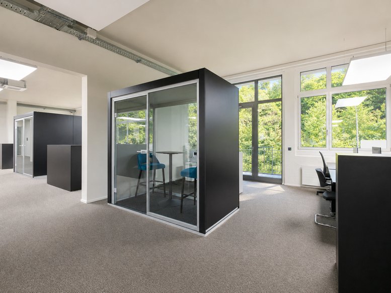 Meeting pod with high chairs at 33b, Albisstrasse, featuring large windows and natural light.