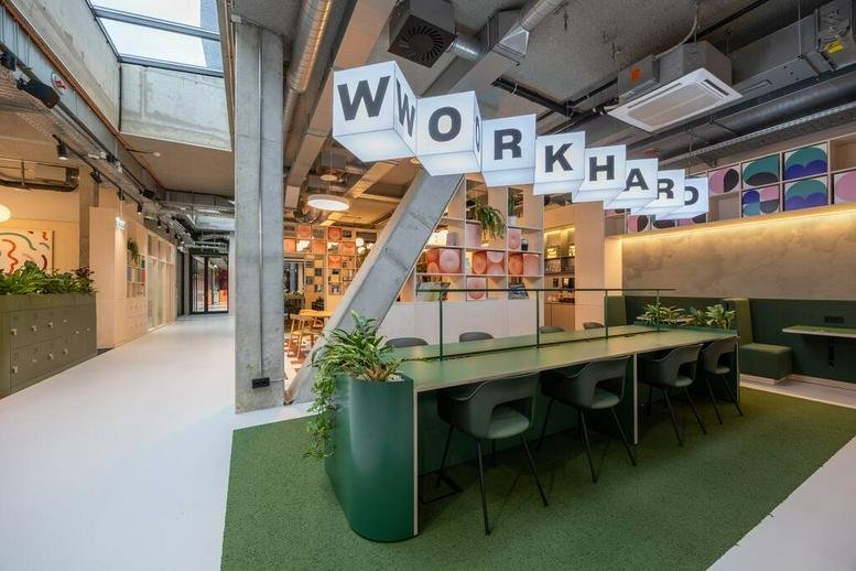 Spacious coworking area at 36, Am Tabor with green desks, hanging plants, and Work Hard signage.