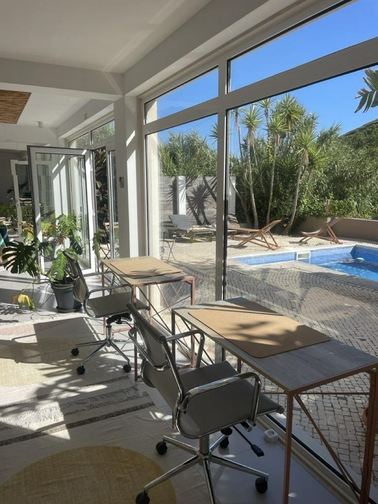 Bright sunlit workspace at 37, Rua da Botelha, Carvoeira with desks overlooking a pool.