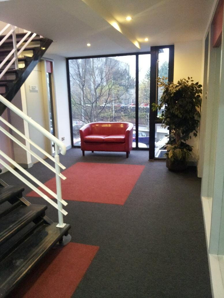 Bright lobby at 40-42 Lisburn Road with a red leather loveseat, large window, and staircase.
