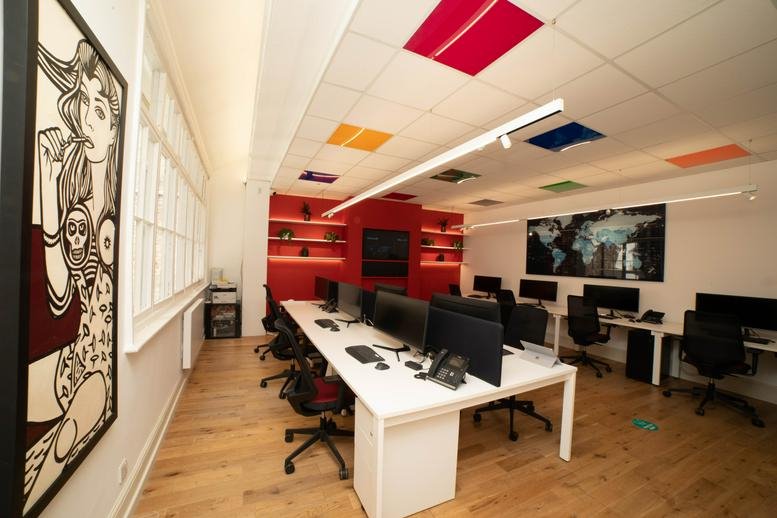 Spacious open-plan office with white desks and a red feature wall.
