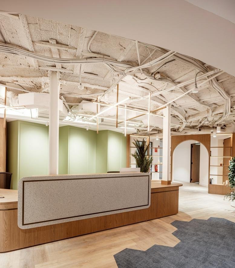 Modern reception desk at 56, Passeig de Gràcia, with a textured front and industrial ceiling.