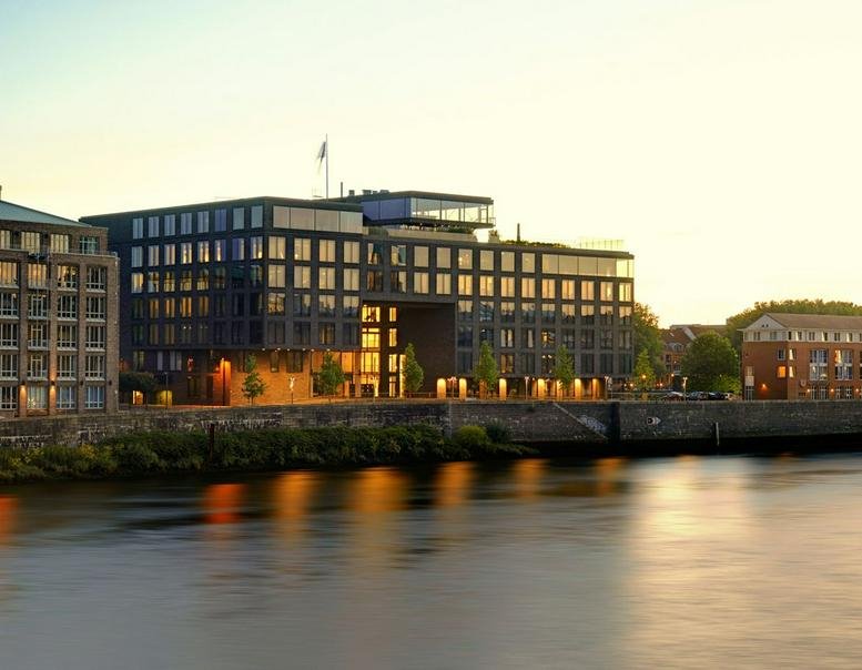 Exterior view of the dark-brick building 59, Teerhof at dusk with river reflections.