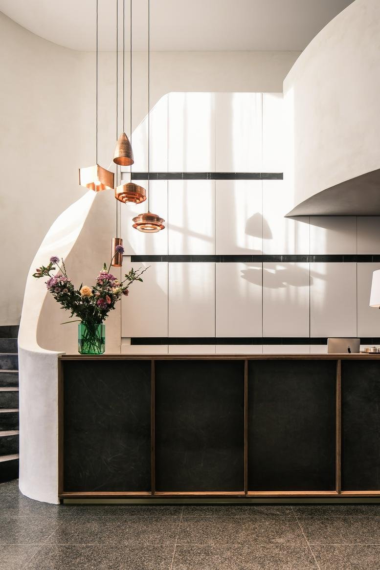Reception area at 6, Avenue des Arts featuring a dark stone desk and copper pendant lighting.