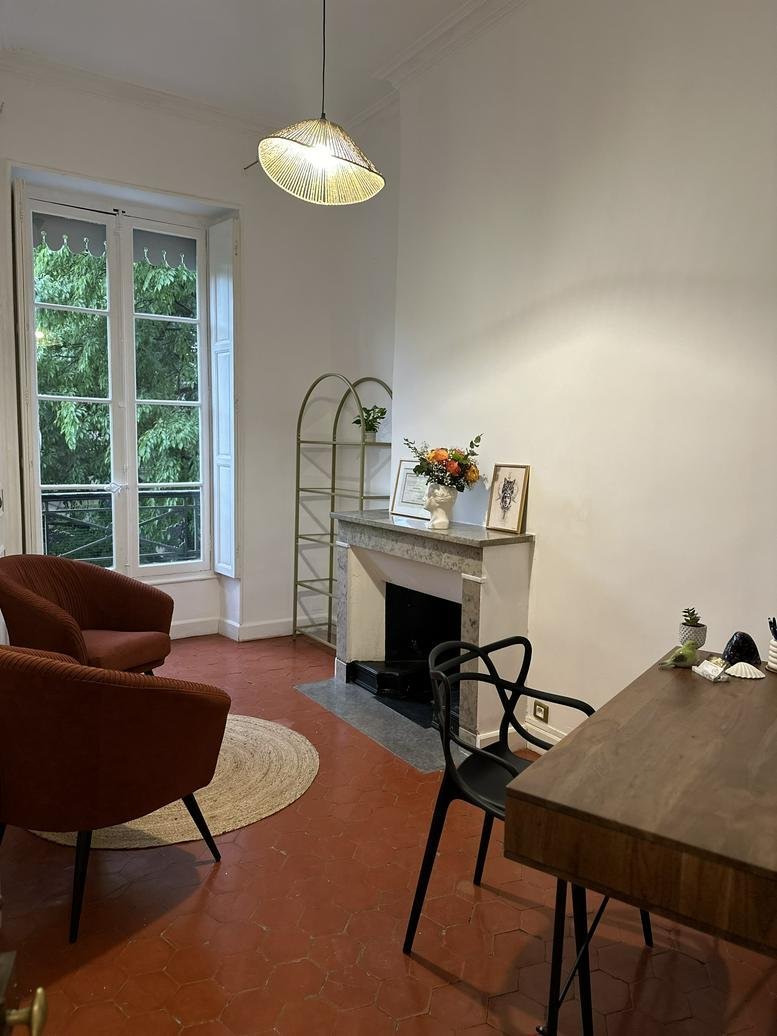 Bright workspace at 6, Rue de la Monnaie with velvet armchairs, a fireplace, and garden views through tall windows.